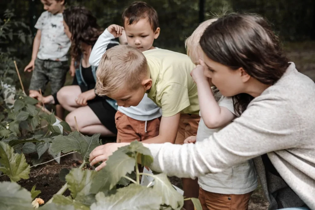 Kinder und Erzieherin entdecken gemeinsam Pflanzen und Gemüse im naturnahen Garten der Kita.
